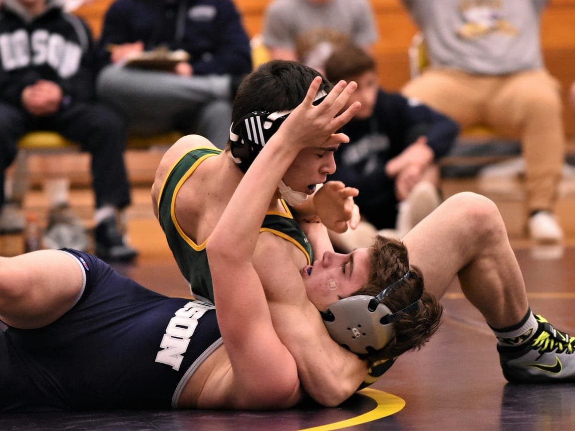 A high school wrestler controls his opponent on the mat.